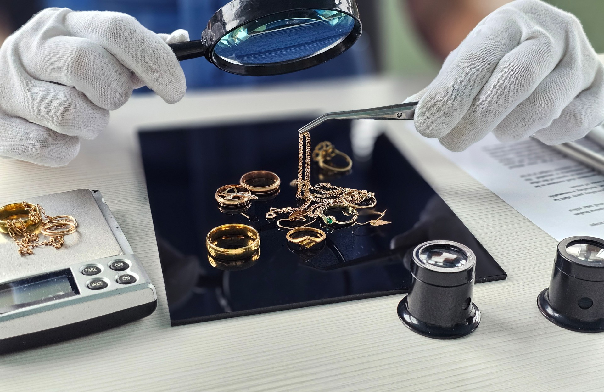 Expert evaluates various gold jewelry pieces with magnifying glass and tweezers