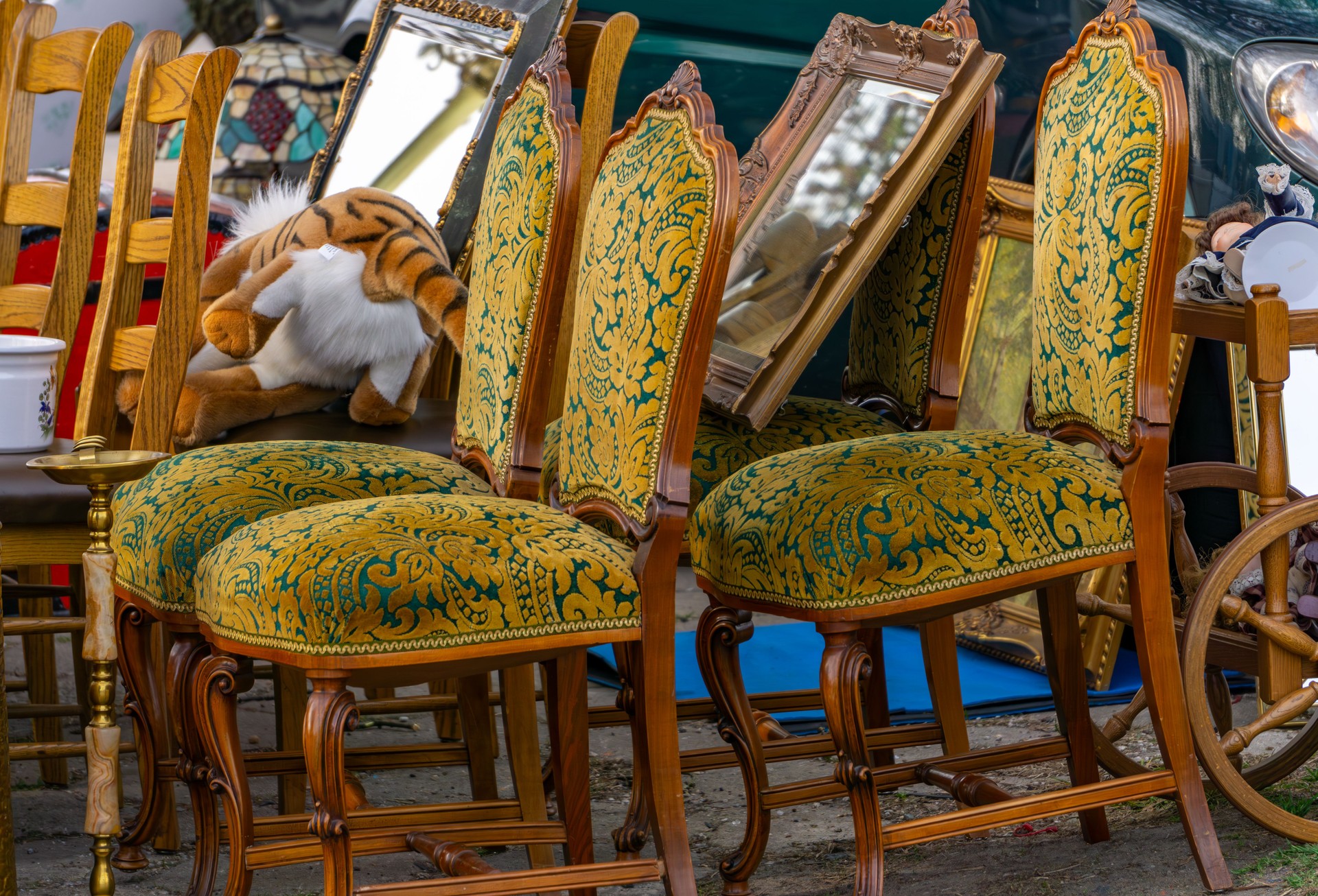 outdoor flea market. A colorful collection of antique chairs with intricate green and gold upholstery, surrounded by mirrors, wooden furniture